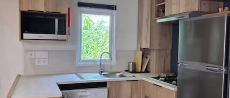 Une cuisine moderne avec des meubles en bois, un réfrigérateur en acier inoxydable, un four à micro-ondes encastré et une fenêtre qui laisse entrer la lumière naturelle.