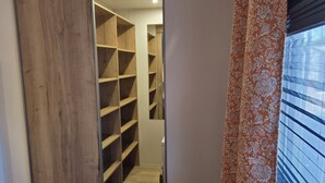 Ein Flur, der zu einem Abstellraum mit mehreren Regalen, einer Holztür und einem Fenster mit Jalousien führt.