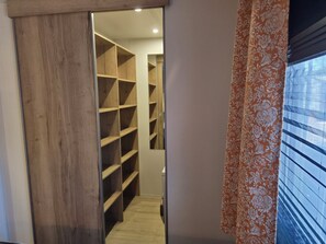 A hallway leading to a closet with multiple shelves, a wooden door frame, and a window with blinds. - High-End Mobile Home on the French Riviera (Fréjus)