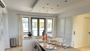Een moderne keuken met een centraal eiland, veel natuurlijk licht door grote ramen en uitzicht op buiten.