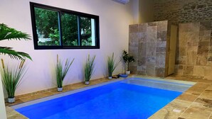 A swimming pool with a blue floor, surrounded by potted plants and a stone wall. - Chambre L'Écrin Végétal - Château, indoor pool & spa (Varennes-Vauzelles)