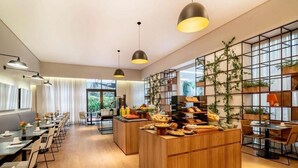 Un comedor de hotel moderno con mesas largas, un buffet central e iluminación colgante.