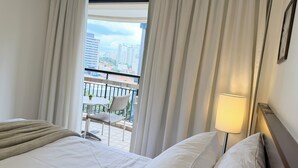 Habitación de hotel con cama, lámpara de noche y vistas a un balcón con una silla y una mesa.