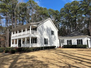 A large white two-story house with a balcony, surrounded by tall trees. - 2026 Masters Week Rental (Grovetown)
