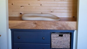 Une chambre à coucher avec une tête de lit en bois, une table de chevet blanche, une commode bleue avec des tiroirs et deux paniers en osier.