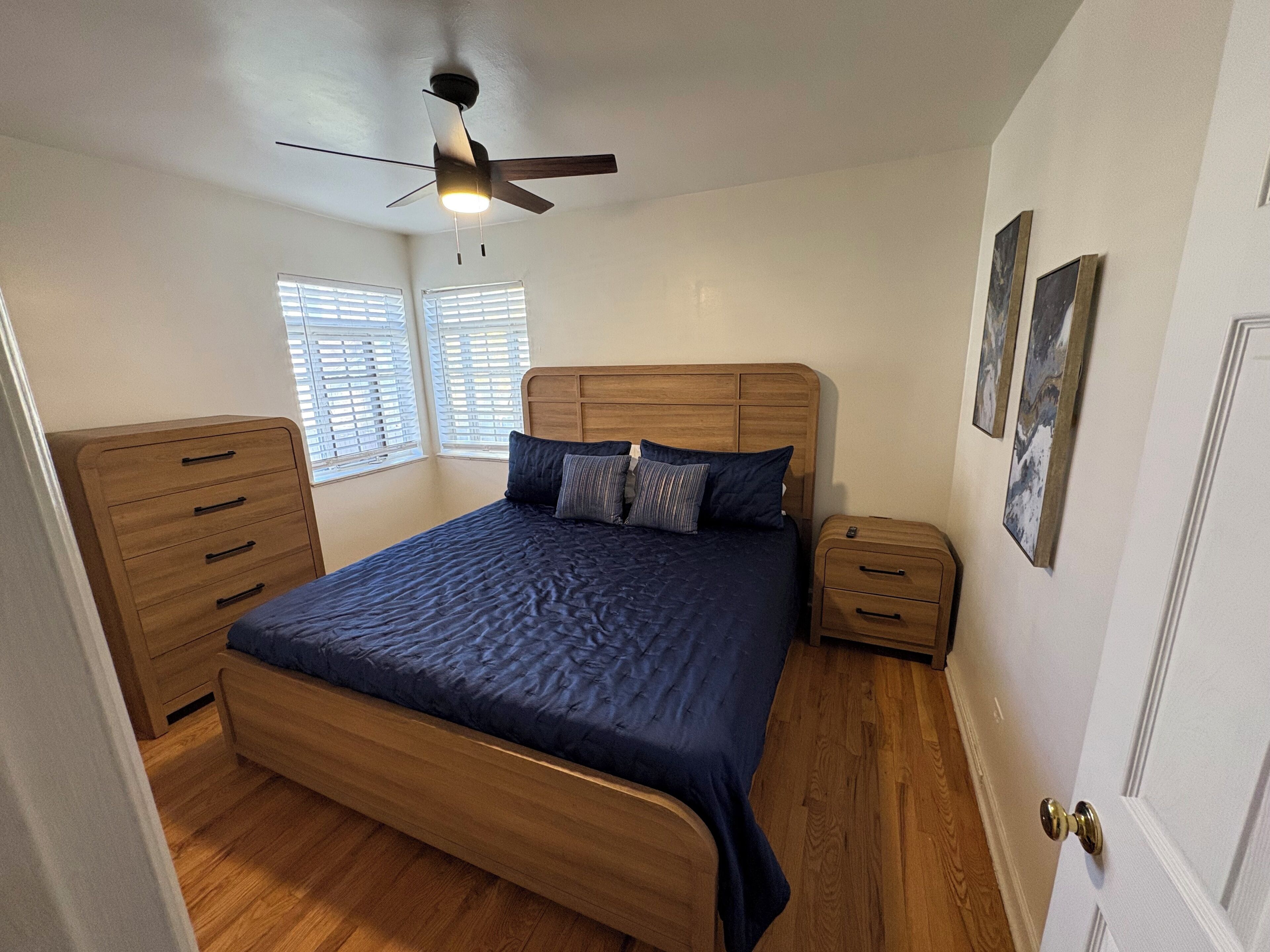 A bedroom with a wooden bed, a nightstand, a dresser, and a ceiling fan.