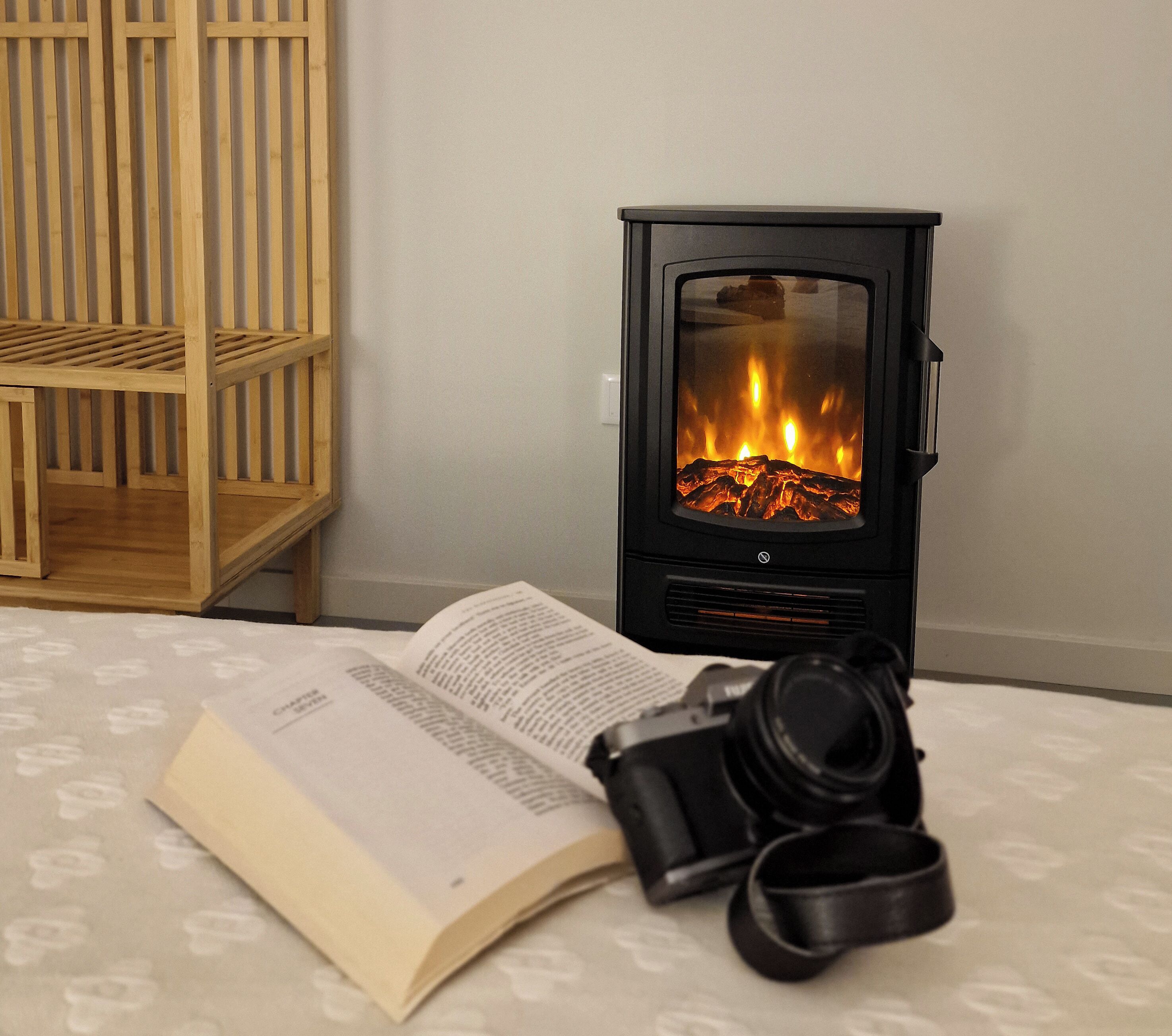Una habitación con una estufa de leña, una estantería, un libro abierto y una cámara.