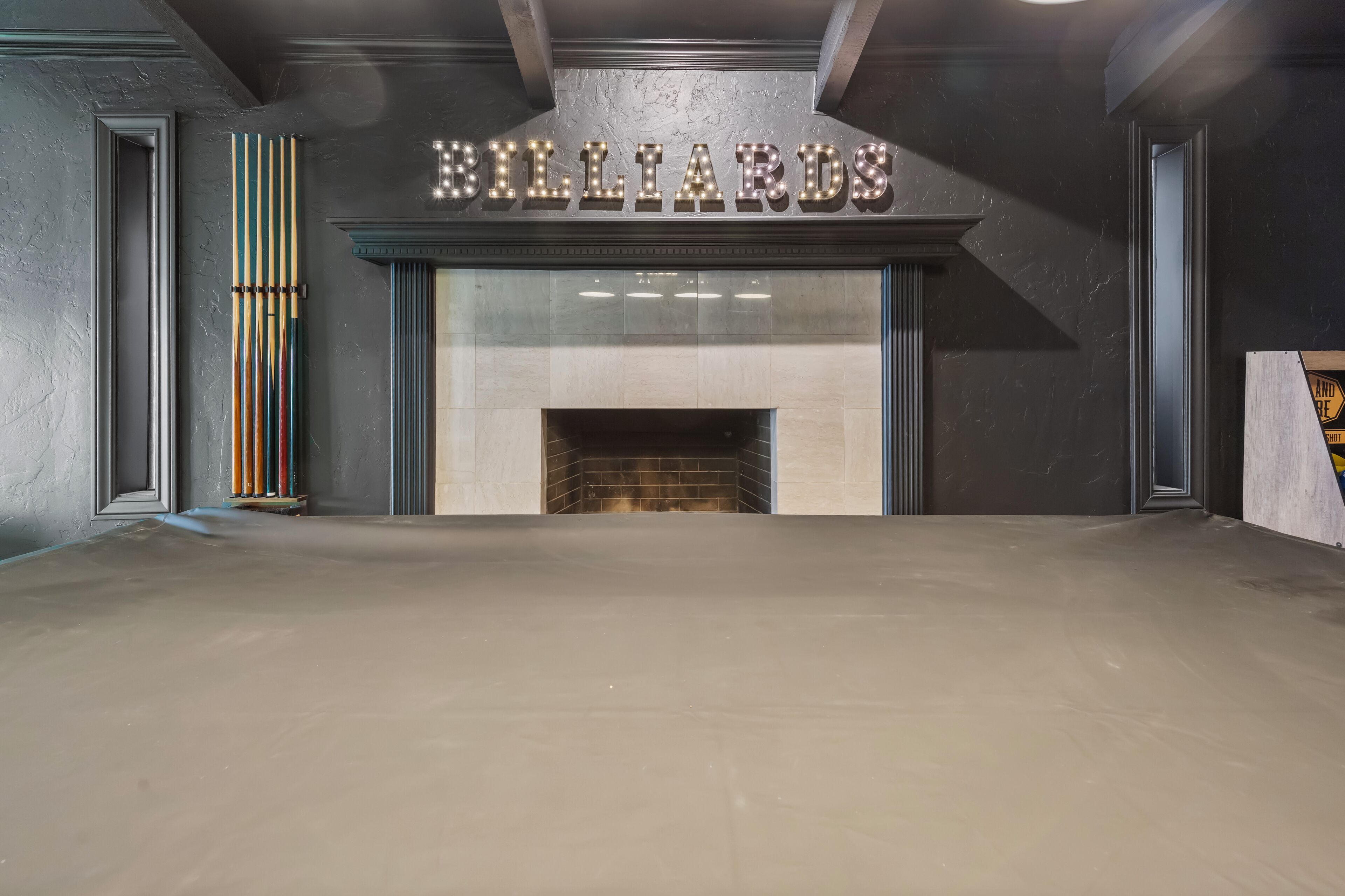 Une salle de billard équipée d’une cheminée, d’une table de billard et d’une enseigne au-dessus de la cheminée sur laquelle on peut lire « BILLARD ».