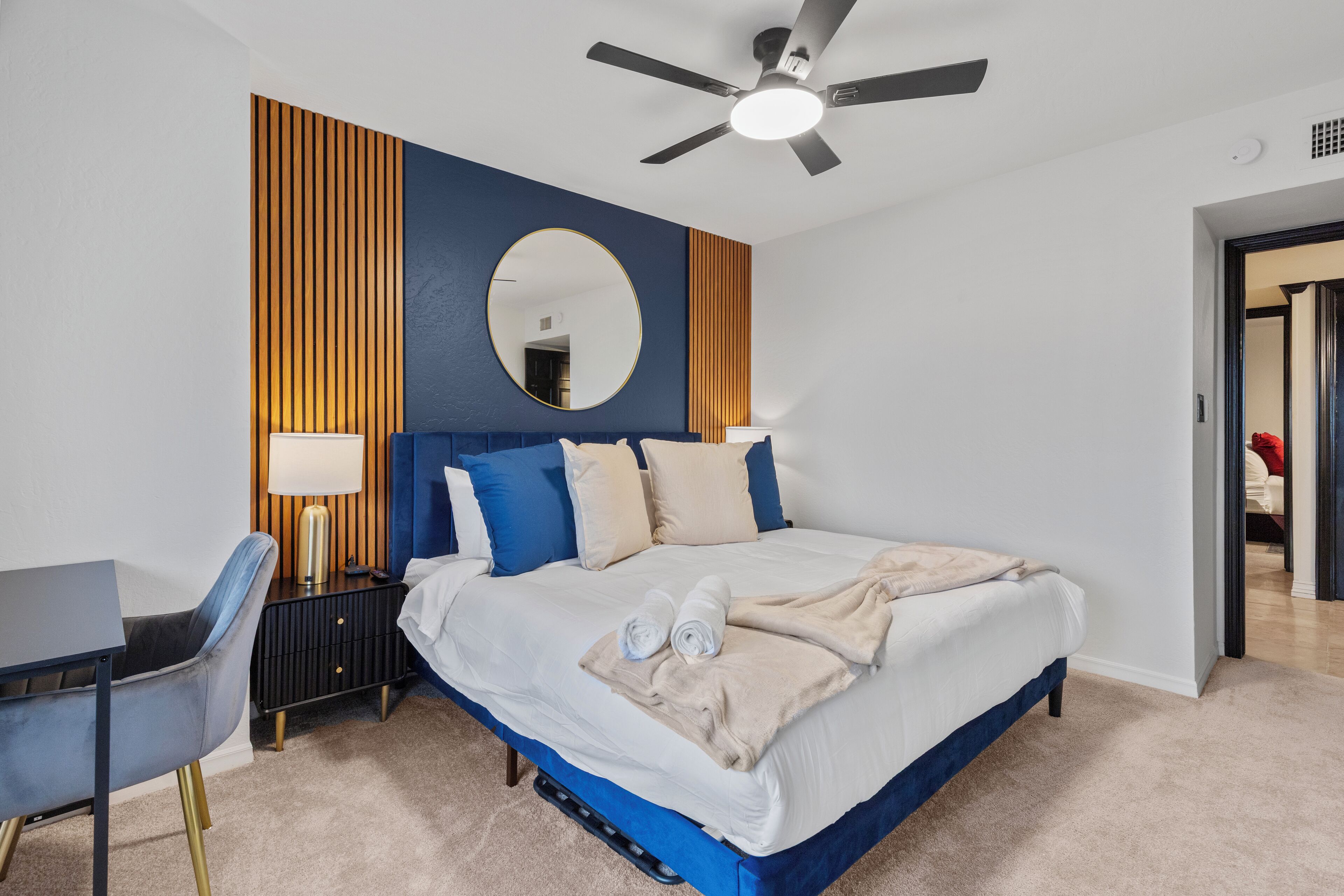 Una habitación de hotel con cama, escritorio, silla, ventilador de techo y espejo.