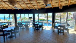 A restaurant with large windows overlooking a pool and the ocean. Tables and chairs are arranged indoors. - Baja 404 Las Palmas Beachfront Resort (Puerto Peñasco)