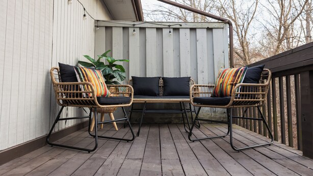 Een houten terras met rieten meubels en een potplant.