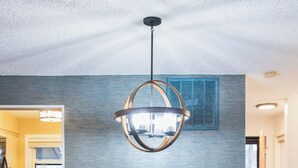 Een eetruimte met een donker houten tafel, zes stoelen en een roze fauteuil met een metalen ring. Daarboven hangt een moderne hanglamp.