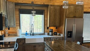 Une cuisine dotée de meubles en bois, d’un réfrigérateur en acier inoxydable, d’un plan de travail en granit et d’une fenêtre donnant sur les arbres.