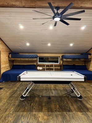 Une petite pièce avec un lit superposé, un ventilateur de plafond et une table surmontée d’un matelas.