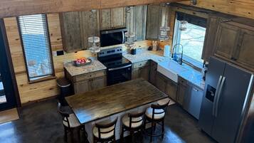 A high-ceilinged kitchen with wooden walls, a central island with stools, a refrigerator, and a microwave.