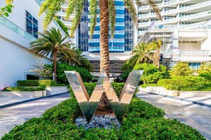 Un edificio moderno con fachada de vidrio, palmeras y una escultura central.