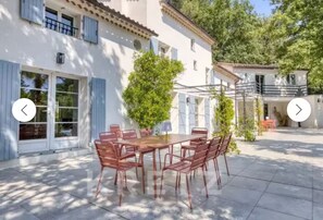 A patio with a wooden table and chairs, surrounded by a white building with blue shutters and a balcony. - Villa Madone - Valbonne (Valbonne)