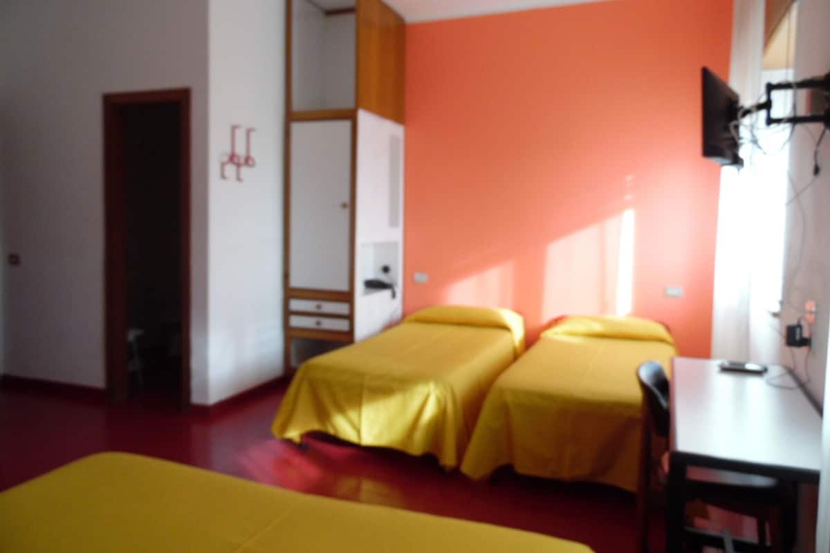 A room with two beds, a desk, and a chair. There is a wardrobe and a television on the wall.