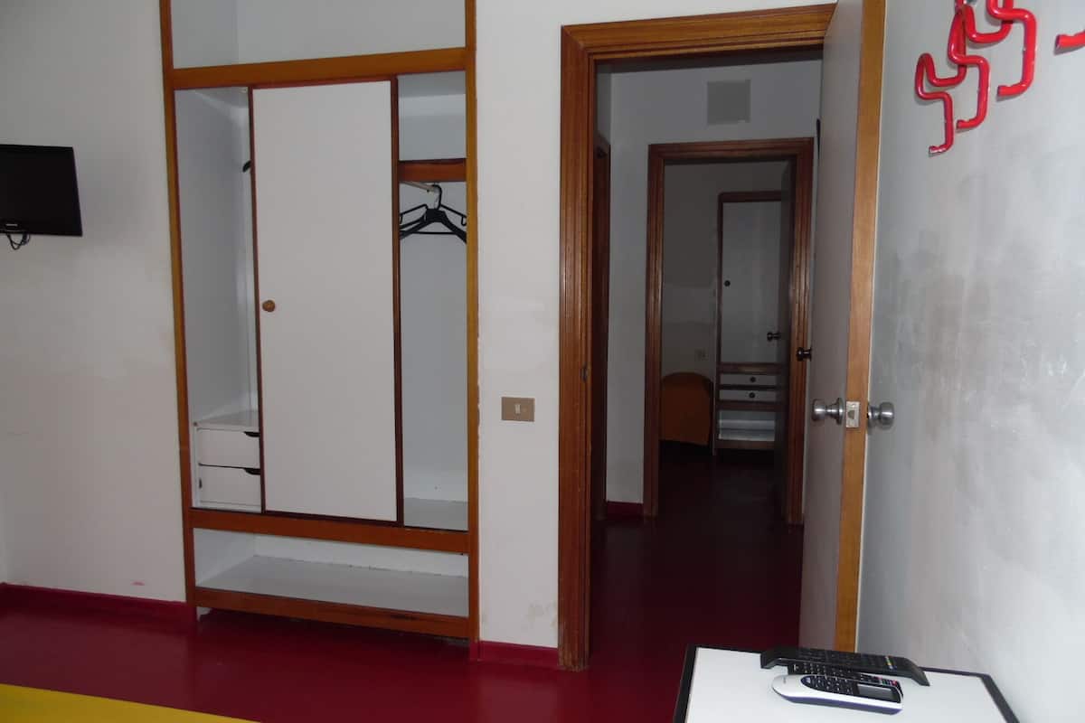 A room with a bed, a desk with a computer, a wardrobe, and a door leading to another room.