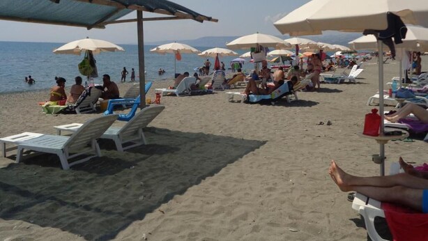 Une plage avec des transats et des parasols, des gens qui se détendent, et la mer en arrière-plan.