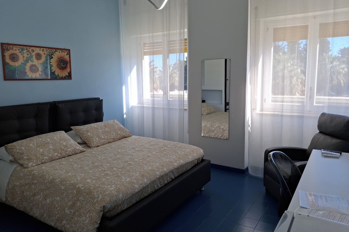 A bedroom with a bed, a chair, a desk, a mirror, and a window with curtains.