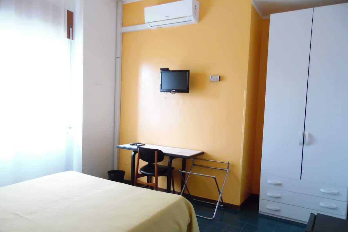 A room with a bed, a desk, a chair, a television mounted on the wall, and a wardrobe.