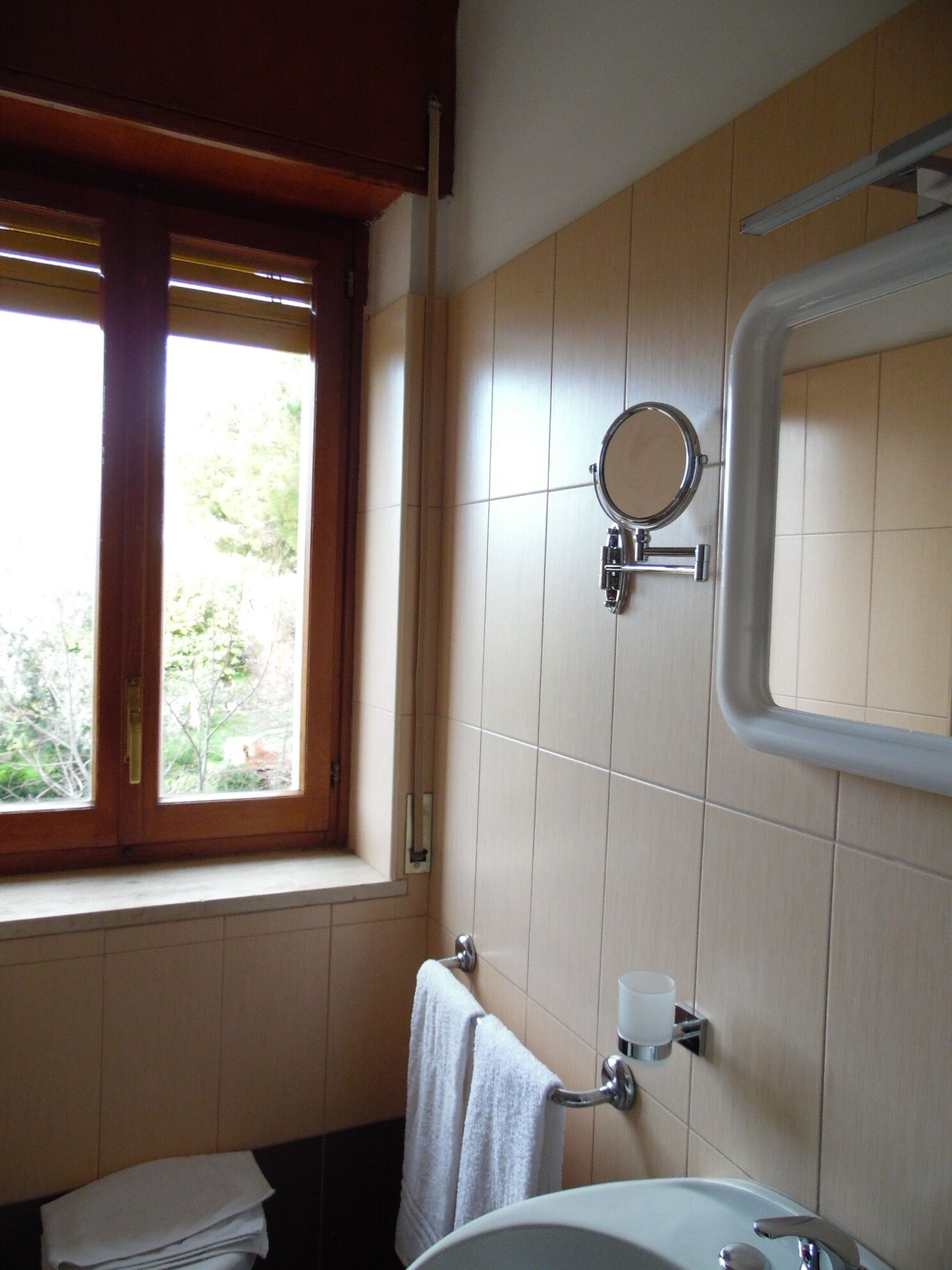 A bathroom with a window, a mirror, a sink, and a towel rack.