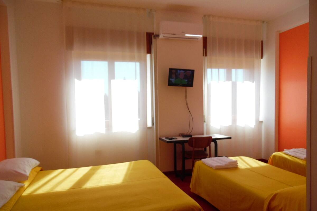 A hotel room with two beds, a desk, a television, and a window with curtains.