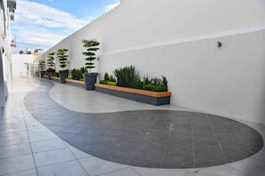 A modern outdoor corridor with a curved pathway, potted plants, and a white wall. - Condo in Centro histórico de Guadalajara Downtown w/parking and pool (Guadalajara)