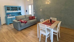 A modern living room with a grey sofa, a dining table with white chairs, and a blue cabinet with glass doors. - SORRENTO POSITANO AMALFI COAST "I VELIERI SUNSET SUITE" (VICO EQUENSE)