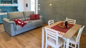 A dining area with a table set for two, a grey sofa with red cushions, and a blue cabinet with dishes. - SORRENTO POSITANO AMALFI COAST "I VELIERI SUNSET SUITE" (VICO EQUENSE)