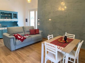 A dining area with a table set for two, a grey sofa with red cushions, and a blue cabinet with dishes. - SORRENTO POSITANO AMALFI COAST "I VELIERI SUNSET SUITE" (VICO EQUENSE)