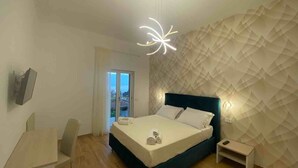 A modern bedroom with a bed, bedside table, and a view of the city through a large window. - SORRENTO POSITANO AMALFI COAST "I VELIERI SUNSET SUITE" (VICO EQUENSE)