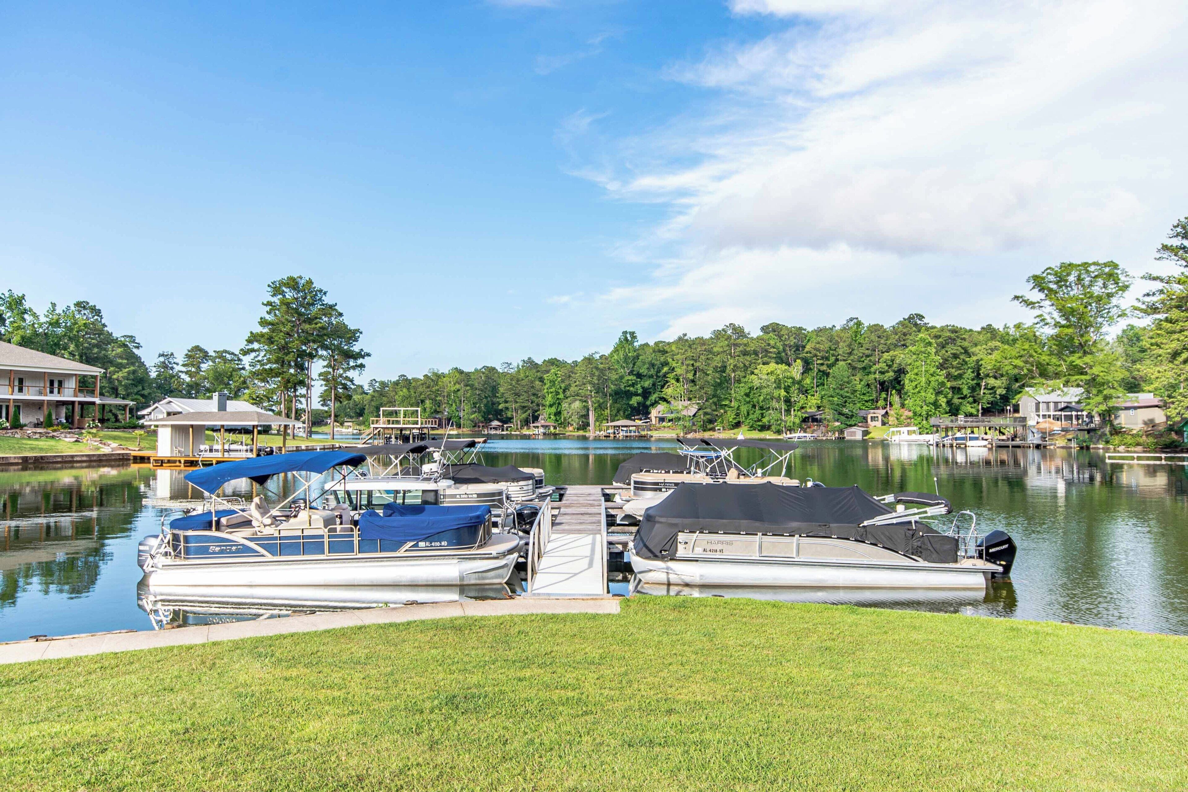 Un port de plaisance avec des bateaux amarrés, une zone herbeuse au premier plan et un lac bordé d’arbres à l’arrière-plan.