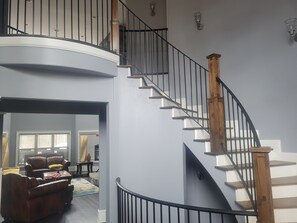 A spacious living room with a curved staircase, leather furniture, and a view of the adjacent room. - Spacious 9-bedroom house in lovely Locust Grove with AC (Locust Grove)
