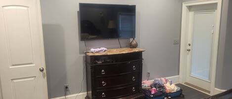 Una habitación con un aparador de madera oscura, un televisor colgado en la pared y una maleta en el suelo.