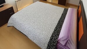 Un dormitorio con cama, armario, radiador, televisor y ventana.