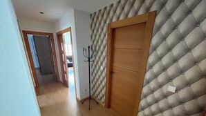 Un pasillo con suelo de madera, una puerta con panel tapizado y un perchero.