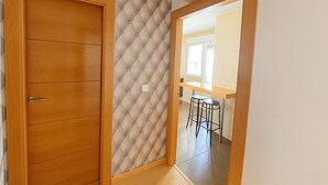 Una habitación con puerta de madera, pared con capitoné y una zona de cocina con un taburete de bar.
