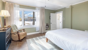Ein Schlafzimmer mit Bett, Stuhl, Kommode, Fenster mit Vorhängen und Deckenventilator.