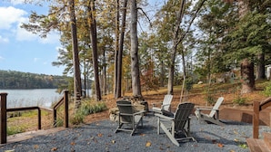Ein Seeufer mit einer Holzterrasse, Adirondack-Stühlen und einem Feuerkorb.