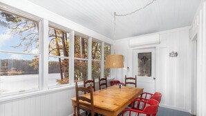 Ein Essbereich mit Holztisch und -stühlen, großen Fenstern mit Blick auf Bäume und einer hängenden Leuchte.
