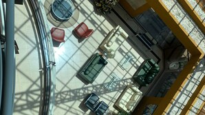 Un vaste atrium doté d’un haut plafond, avec un espace central aménagé en salon, comprenant des tables et des chaises rondes, le tout entouré de sièges rembourrés de couleur rouge et verte.