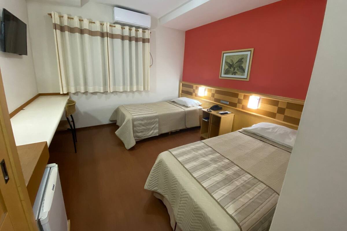 A hotel room with two beds, a desk, a chair, an air conditioner, and a television.