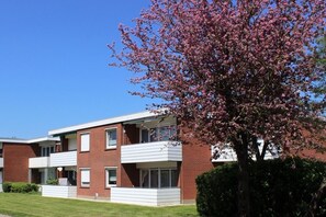 A two-story brick building with a flat roof, large windows, and a balcony on the second floor. - Vacation apartment Urlaubsschmiede 6 EG at the North Sea in Wangerland/ Horumersiel (Wangerland)