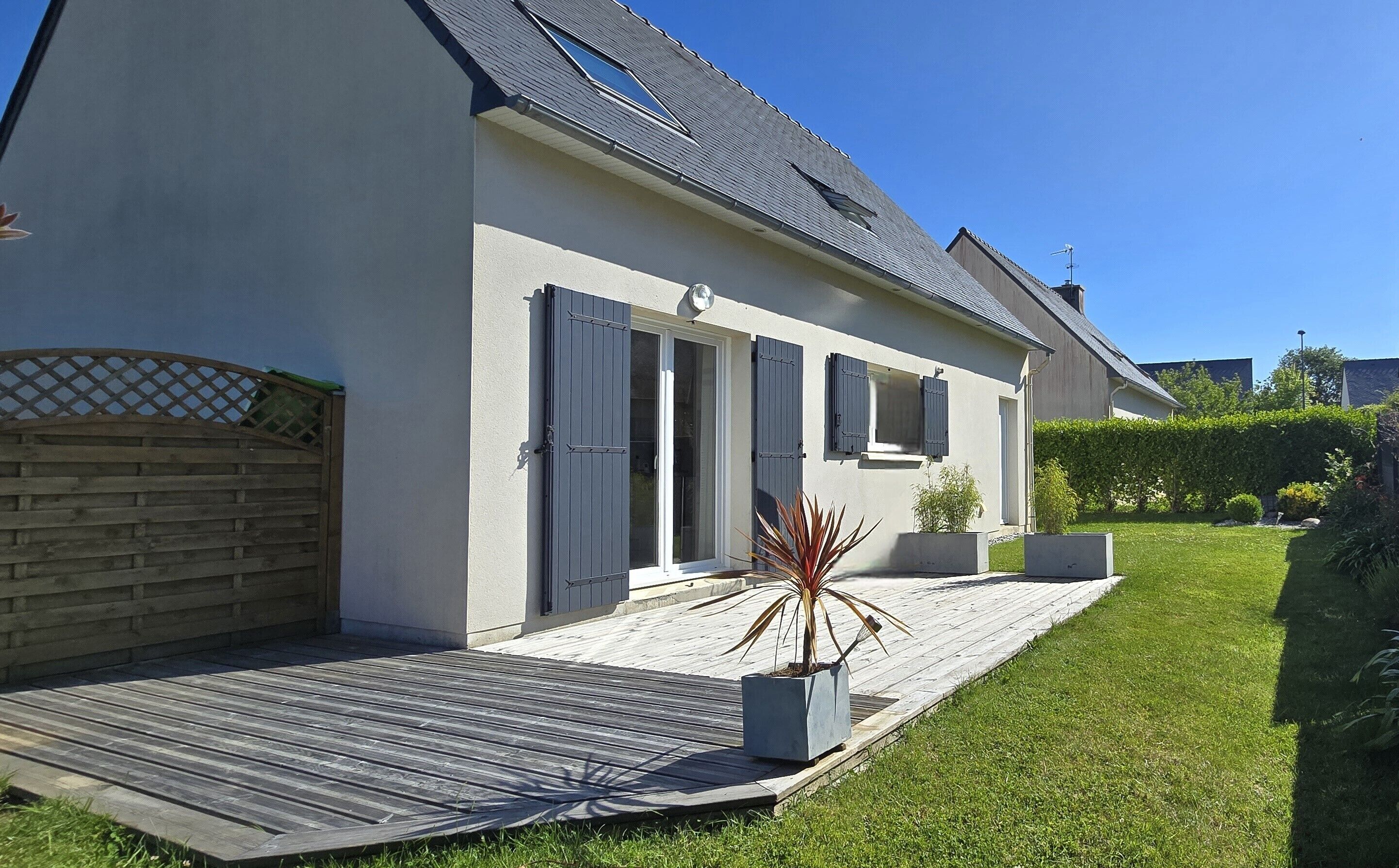 A modern house with a sloped roof, a wooden deck, and a well-maintained lawn.