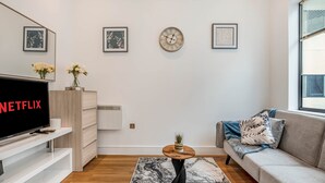 A modern living room with a flat-screen TV, a coffee table, a sofa, and framed artwork on the walls. - The Cosy Luxe (Slough)