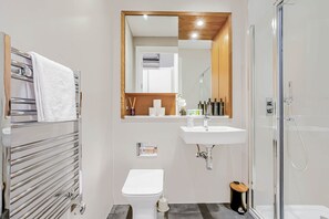 A modern bathroom with a glass-enclosed shower, a white sink, and a towel rack with multiple towels. - The Cosy Luxe - Free Parking - Evara (Slough)