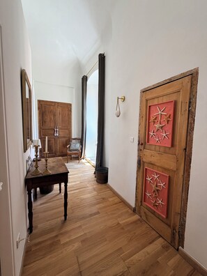 Ein Korridor mit Holzboden, einer Holztür mit Seestern-Dekorationen, einem Spiegel und einem Tisch mit Kerzen.