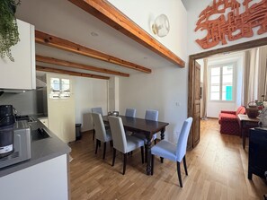 Ein Essbereich mit Holztisch und -stühlen, eine Küche mit modernen Geräten und Blick nach draußen durch eine Tür.